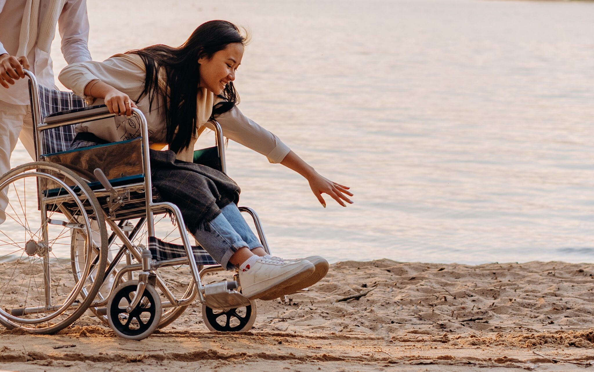 A woman in a wheelchair, being pushed on the beach